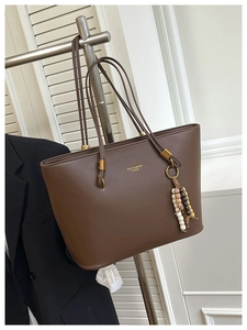 Detail of a dark brown vintage tote bag featuring a leather matte finish and bead tassel