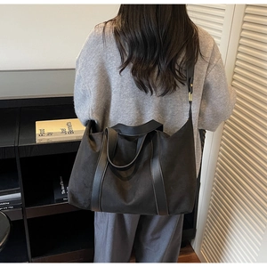 Close-up of a large black tote bag in matte suede texture shown on a female model