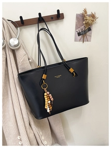 Close-up of black leather tote bag featuring gold lettering and beaded charm detail