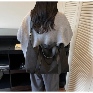 Detail of a large black suede tote bag shown on model in a minimalist indoor setting