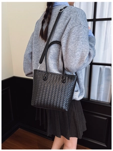 Détail d'un sac seau noir en cuir tressé porté par un mannequin dans un cadre épuré