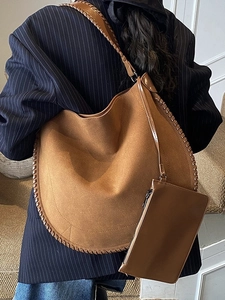 Brown suede tote bag with woven edge and matching pouch, shown on shoulder in interior setting