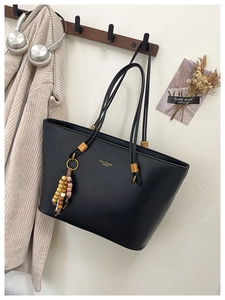 Detail of black faux leather tote with gold FDYJ logo and ethnic beaded tassel charm