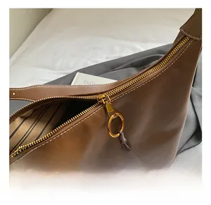 Detailed macro view of gold metal zipper and beaded tassel on brown leather bucket bag