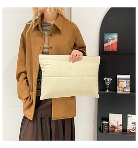 Large beige quilted nylon clutch bag held by a model showing spacious storage capacity