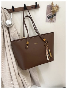 Close-up of a brown matte leather tote bag with stylish beaded charms and metal hardware