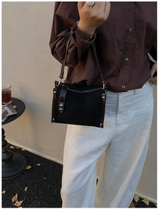 Detail of vintage black and brown leather crossbody bag with silver buckle and rivets