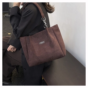Detail view of large brown corduroy tote bag with silver chain strap and logo patch