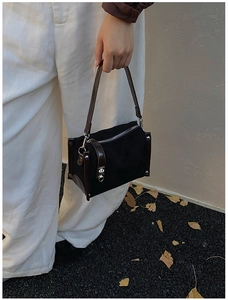 Outdoor shot of a black matte textured handbag with brown leather trim and silver metal zip