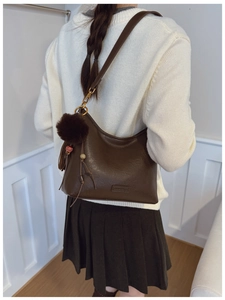 Detail view of large dark brown leather hobo bag with tassel and pom-pom charm
