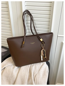 Detailed close-up of dark brown faux leather tote bag with gold logo and beaded charm