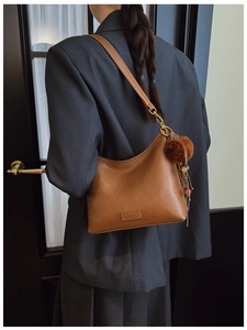 Detail of vintage brown leather shoulder bag with gold hardware and plush pom-pom charm