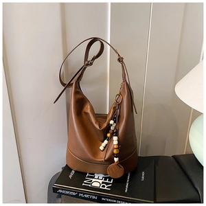 Detail of caramel brown leather hobo bag with unique wooden bead charm on a book
