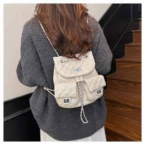 Detail of cream quilted backpack featuring silver chain straps and twin front pockets