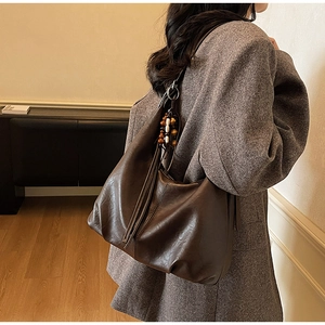 Detail of dark brown leather tote with long tassel and vintage wooden bead charm