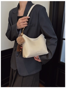 Close-up of cream PU leather shoulder bag with gold hardware and a brown fur pompom detail