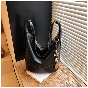 Detail of black leather tote bag with white contrast stitching and vintage beaded charm