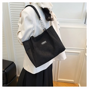 Détail du sac cabas noir avec bandoulière en chaîne et écusson de marque minimaliste