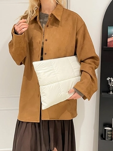 Brown suede shirt jacket paired with a white quilted puffer clutch bag in minimalist style