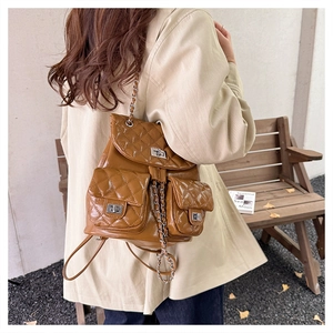 Detail of caramel brown quilted backpack with silver buckles and chain straps outdoors