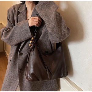 Detail view of large dark brown retro tote bag with wooden bead tassel on a model