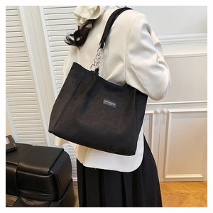 Detail shot of black suede tote bag with stylish gold chain strap and rectangular logo patch