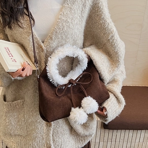 Détail du sac en daim marron foncé avec poignée en fausse fourrure blanche et pompons