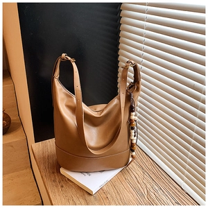 Detail of a brown leather tote bag with boho wooden bead charm on a wooden bench