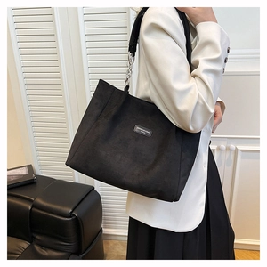 Detail of black suede tote bag with thick silver chain link strap on model