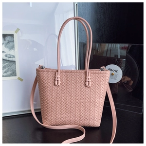 Détail d'un sac seau rose tressé montrant la texture et les poignées délicates