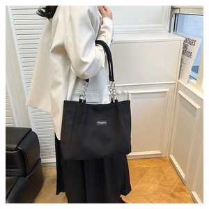 Model wearing a black matte tote bag with silver chain straps and brand logo patch