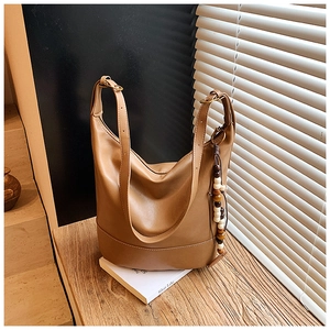 Detail of caramel faux leather hobo bag with vintage bead pendant on wooden bench