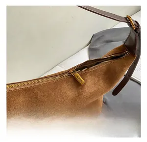 Detail shot of golden metal zipper and brand logo on brown suede shoulder bucket bag