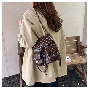 Detail of dark brown quilted leather backpack featuring silver chain straps and turn-lock pockets