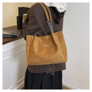 Detail of a brown suede tote bag with chain strap shown in a modern urban lifestyle setting