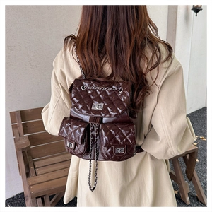 Detail of dark brown quilted backpack with silver buckles and chain straps on a model