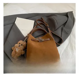 Dettaglio di una borsa a secchiello in camoscio marrone con chiusura in metallo e orsetto