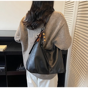 Detail of black leather tote bag with vintage wooden bead tassel on shoulder