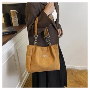 Detail of brown suede tote bag with stylish silver metal chain handles and logo patch