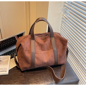 Detail view of large brown suede tote bag with leather straps on a vintage leather seat