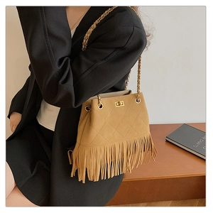 Detail of tan suede bucket bag with quilted patterns, fringe decor, and chain strap