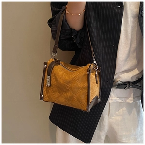 Detail of mustard yellow quilted suede handbag with brown leather trim and metal hardware