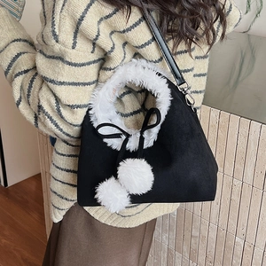 Détail du sac en daim noir avec fourrure blanche et pompons sur pull d'hiver en maille