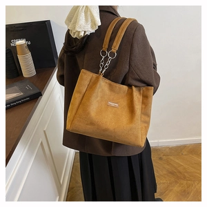 Close-up of caramel brown suede tote bag featuring silver chain strap and brand label
