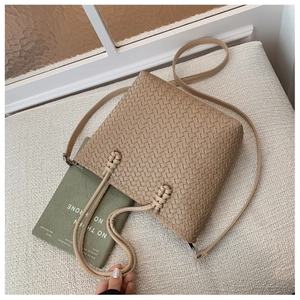 Détail du sac seau beige tissé avec motif en damier minimaliste et détail de nœud supérieur