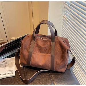 Detail of suede tote bag with leather handles and adjustable strap on a leather seat