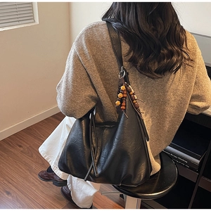 Detail of black leather hobo bag with fringe and wooden bead charm on a model's shoulder
