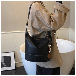 Detail of black leather bucket bag featuring white contrast stitching and wooden bead charm