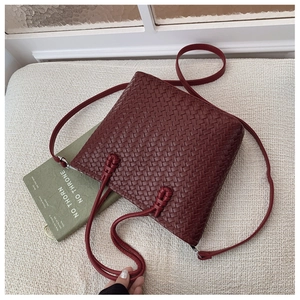 Détail d'un sac seau bordeaux en cuir tressé avec bandoulière nouée sur un support souple