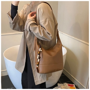 Detail of a brown leather hobo bag with white stitching and decorative wooden beads